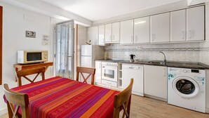 A compact kitchen with a microwave, oven, dishwasher, and washing machine. There is a dining table with chairs and a colorful tablecloth. - Apartment 'Rural Ordiso' with Mountain View, Private Terrace and Wi-Fi (Torla-Ordesa)