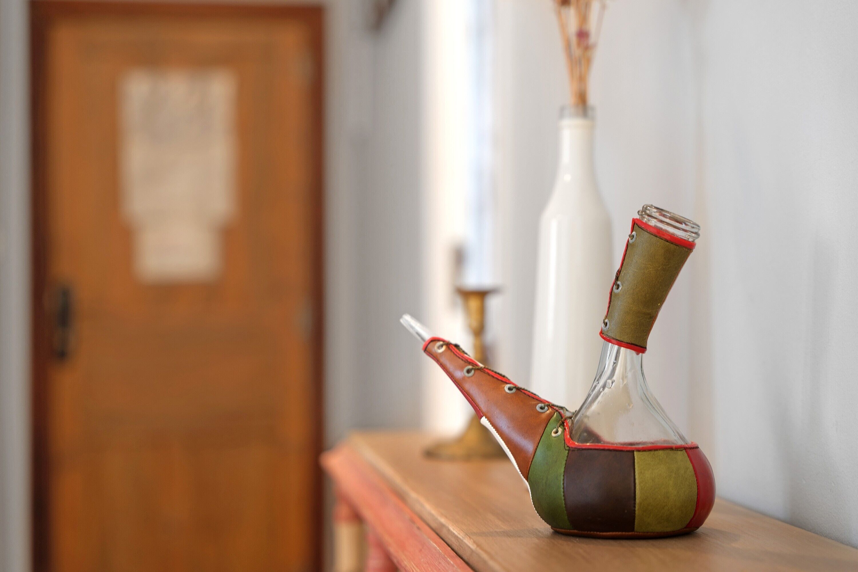 A glass decanter with a leather strap on a wooden surface.