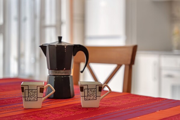 Une table avec deux tasses et une cafetière, le tout posé sur une nappe rouge.