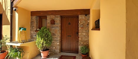 A yellow building with a wooden door, stone walls, and potted plants.