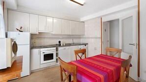 A compact kitchen with white cabinets, a built-in oven, a dishwasher, and a dining area with a table and chairs. - Apartment 'Rural Ordiso' with Mountain View, Private Terrace and Wi-Fi (Torla-Ordesa)