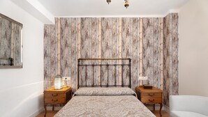 A bedroom with a bed, two nightstands, a white chair, and a wooden headboard. - Apartment 'Rural Ordiso' with Mountain View, Private Terrace and Wi-Fi (Torla-Ordesa)