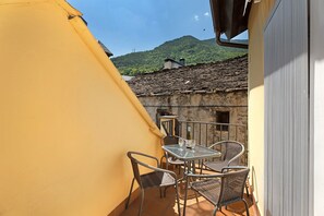 Un balcón con mesa y sillas, una pared amarilla y vistas a la montaña.