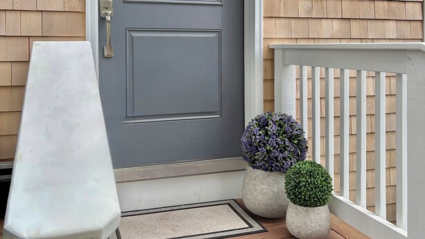 A grey front door with a white mailbox, a small potted plant, and a white railing on a wooden porch. - Brand New Four Bedroom Home Near Beach and Town (Chatham)