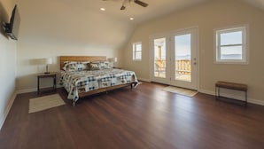 Ein geräumiges Schlafzimmer mit einem großen Bett, einem Deckenventilator und einem Balkon mit einer Holzdielen-Terrasse.