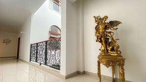 Un vaste hall d’entrée orné d’une statue dorée représentant une figure tenant une balance, d’un garde-corps de balcon en fer forgé décoratif et d’un sol carrelé.