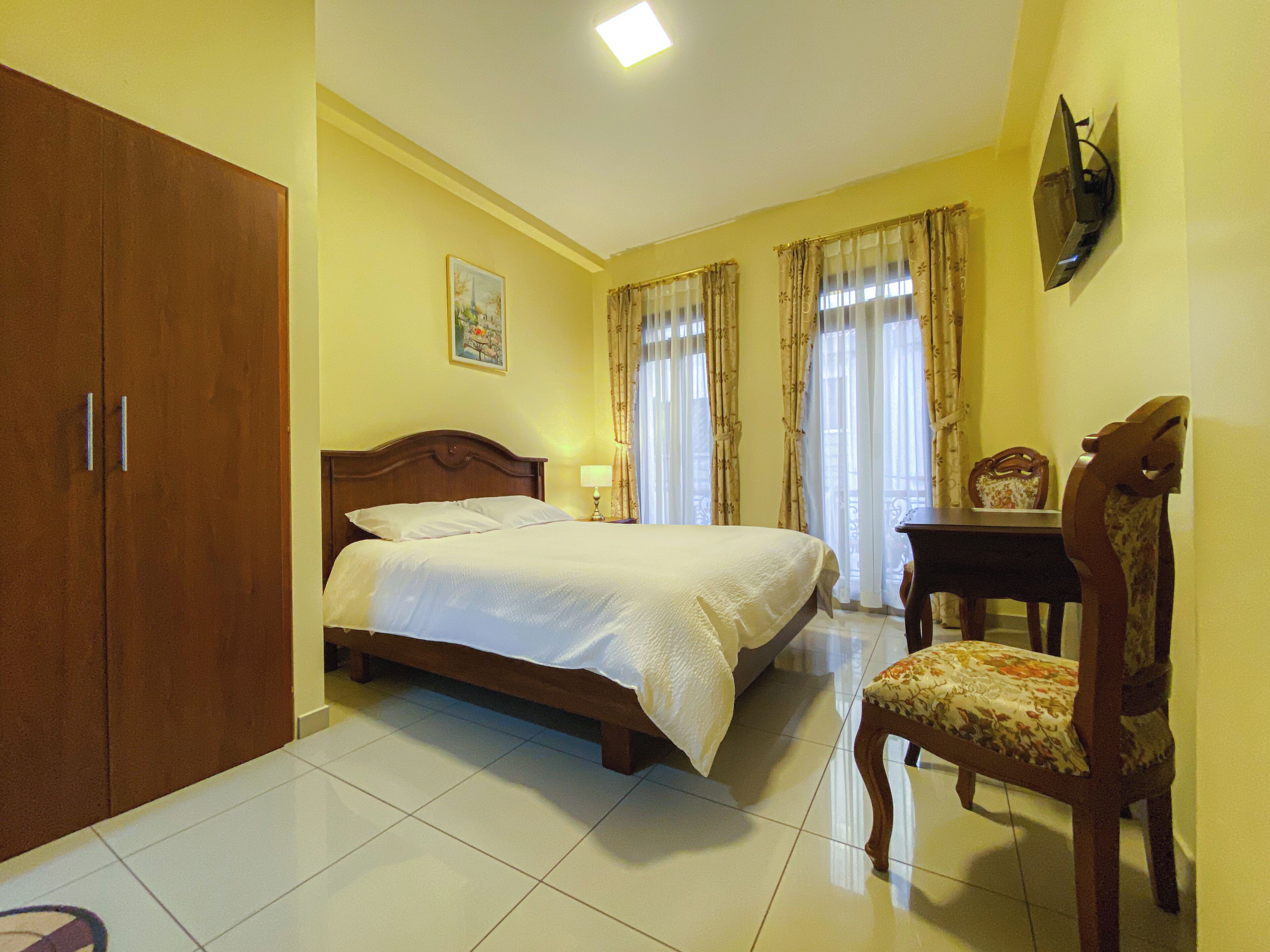 Un dormitorio con una cama doble, un armario de madera, un escritorio con silla y un televisor montado en la pared.