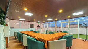 Une salle de conférence avec une longue table, des chaises vertes et un sol carrelé.