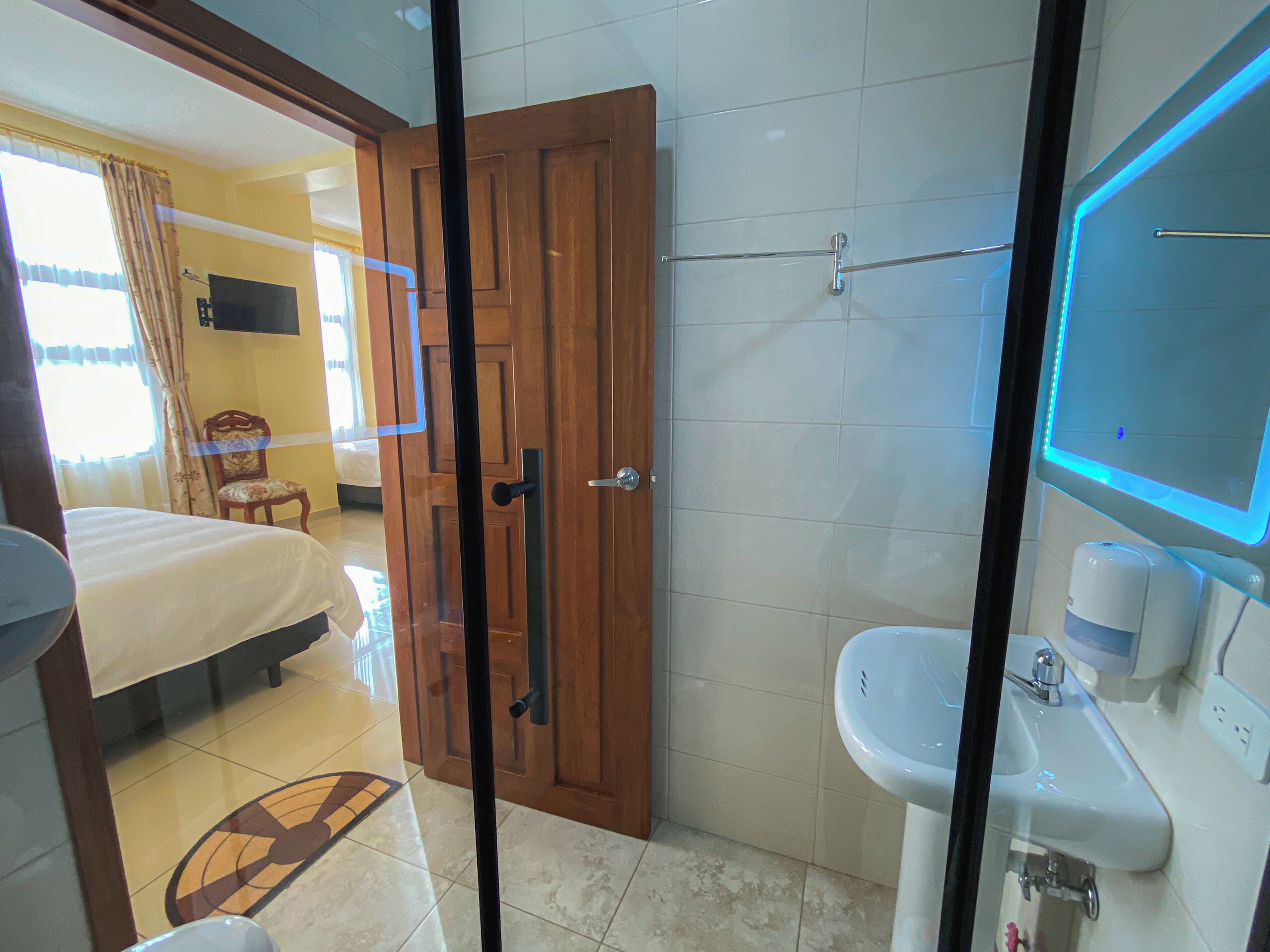 Habitación de hotel con cama, puerta de madera, baño con lavamanos y espejo, y un inodoro.