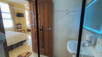 Habitación de hotel con cama, puerta de madera, baño con lavamanos y espejo, y un inodoro.
