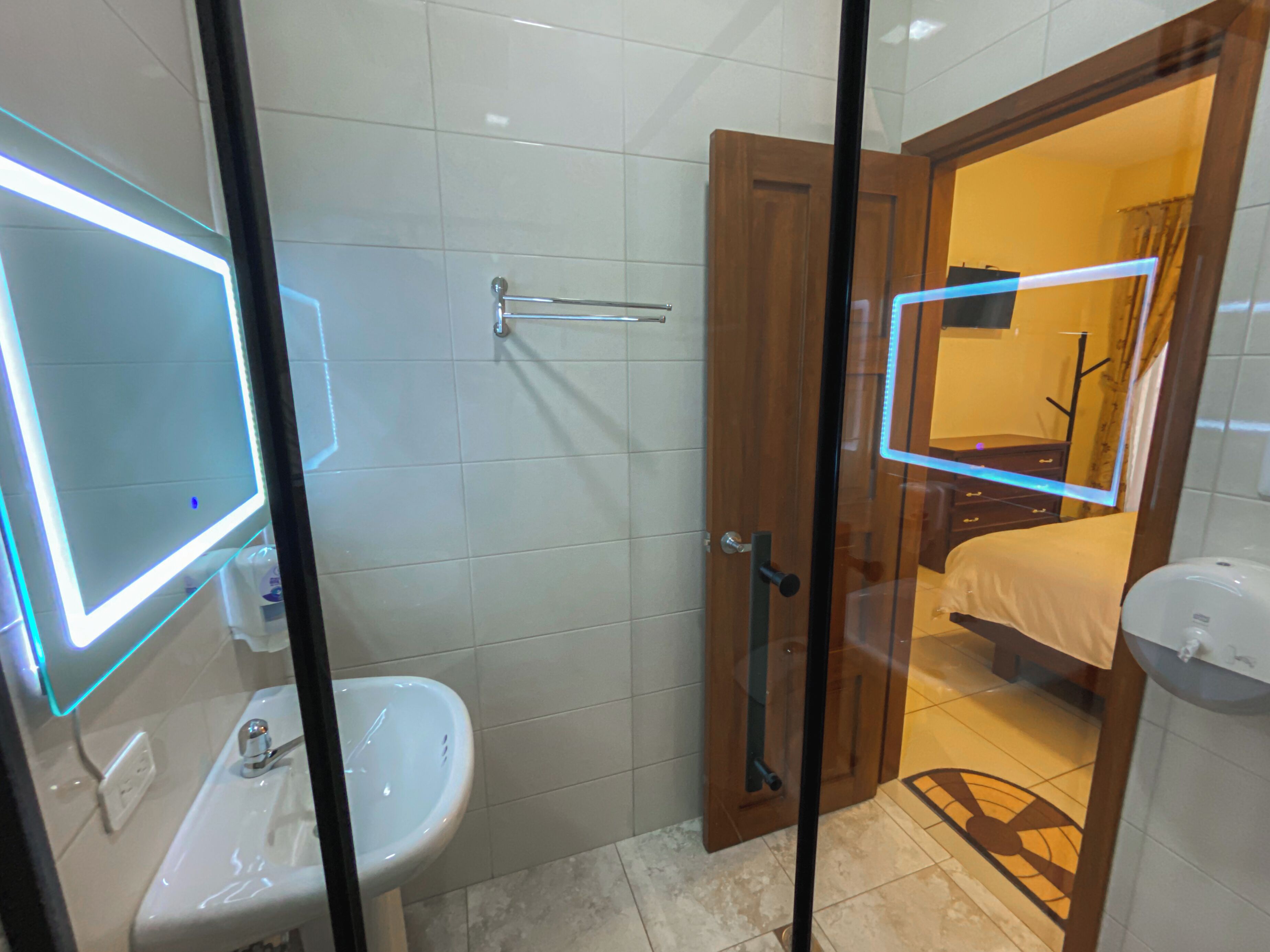 Un baño moderno con cabina de ducha de vidrio, un lavabo blanco y una puerta de madera que da a un dormitorio.