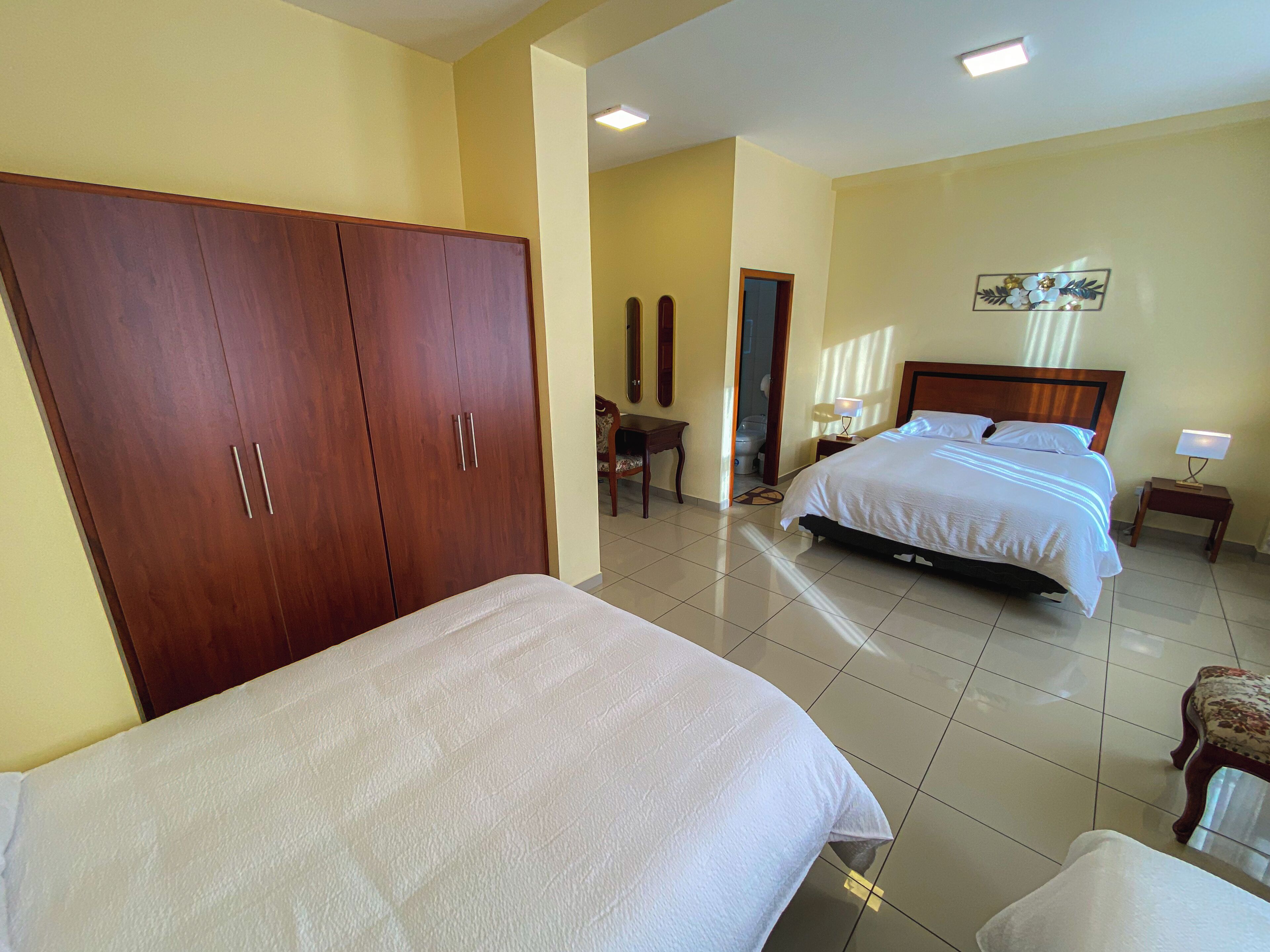 Habitación de hotel con un armario grande, una cama con ropa blanca, una mesita con lámpara y un adorno en la pared.