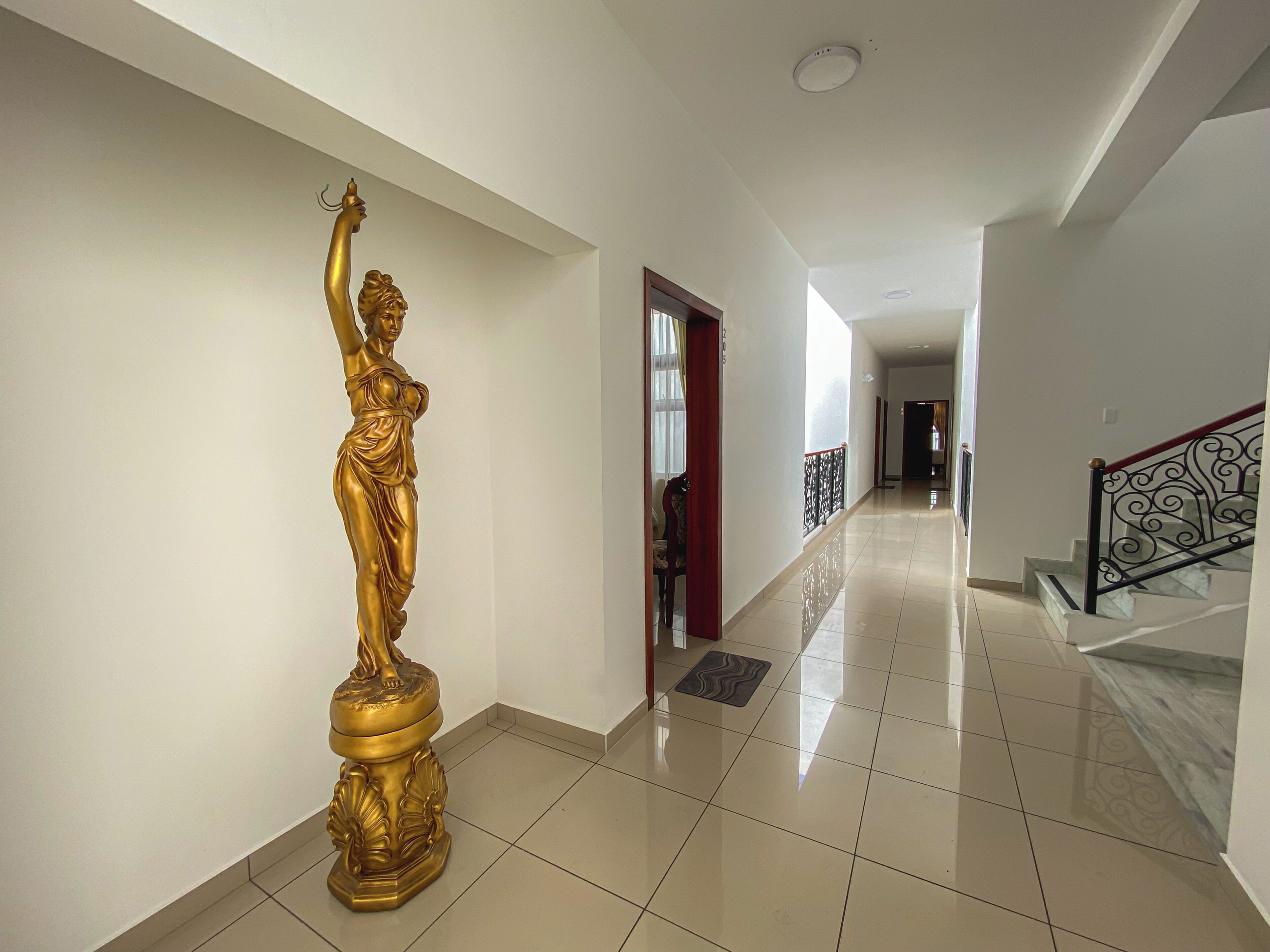 Un pasillo con una estatua dorada, una escalera con barandilla decorativa y suelo de baldosas.