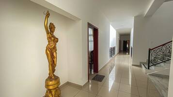 Un pasillo con una estatua dorada, una escalera con barandilla decorativa y suelo de baldosas.