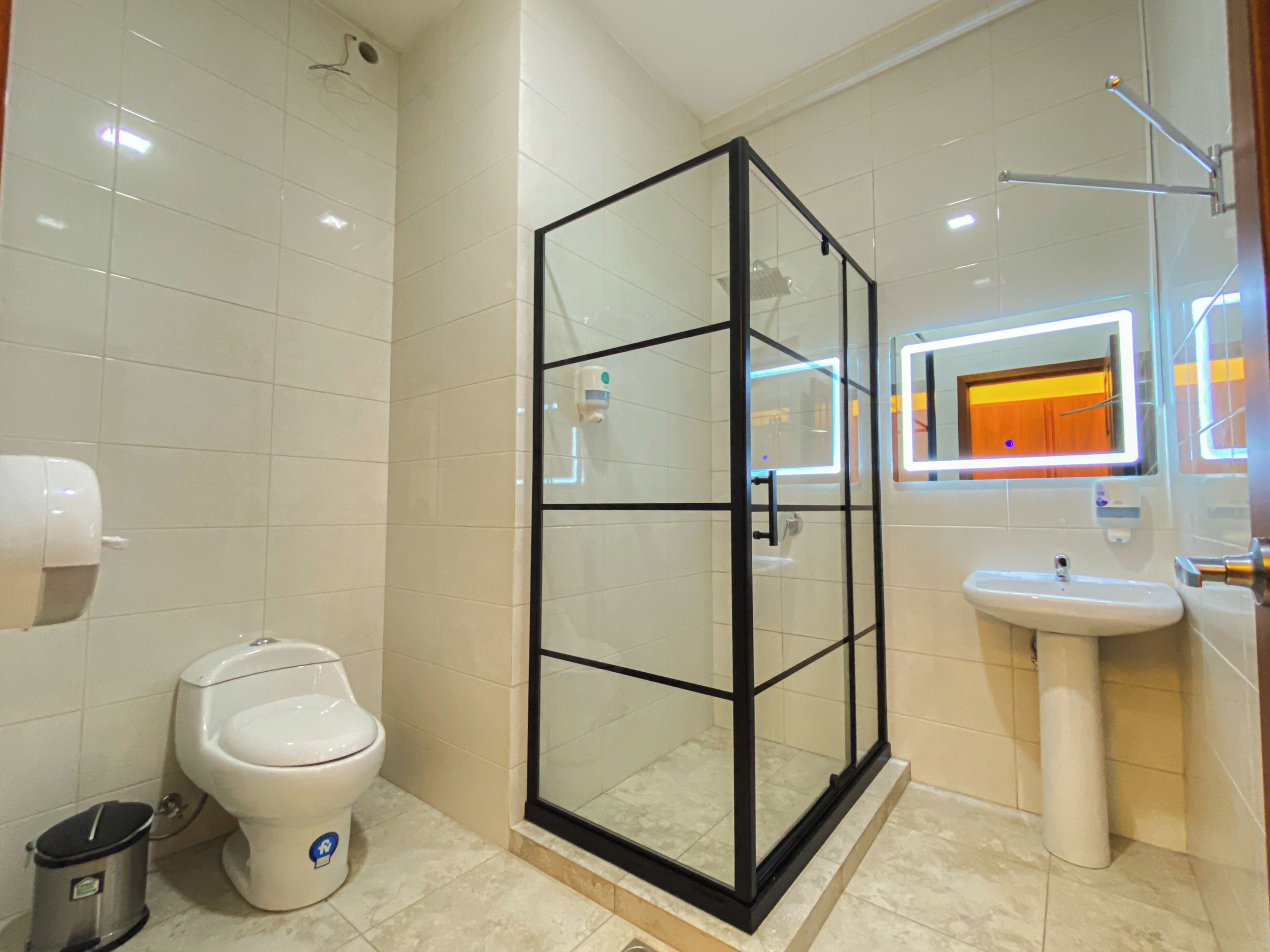 A modern bathroom with a glass-enclosed shower, a toilet, a sink, and a mirror with a neon light.