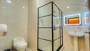 A modern bathroom with a glass-enclosed shower, a toilet, a sink, and a mirror with a neon light.