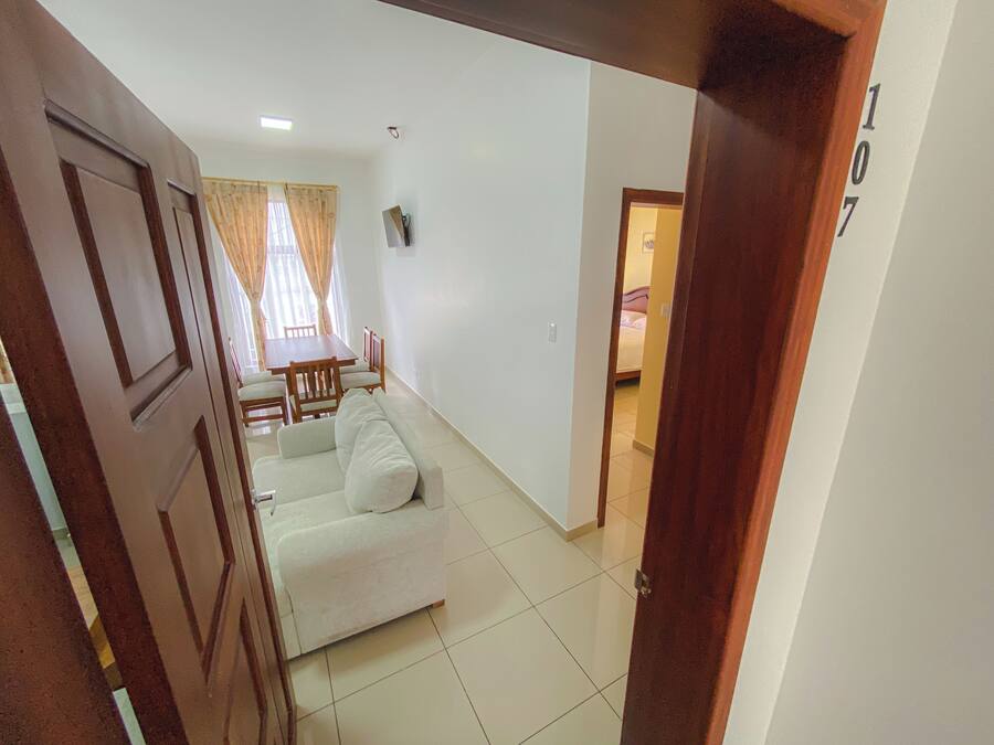 A living room with a sofa, a dining table, and chairs. There is a door with a number on it.