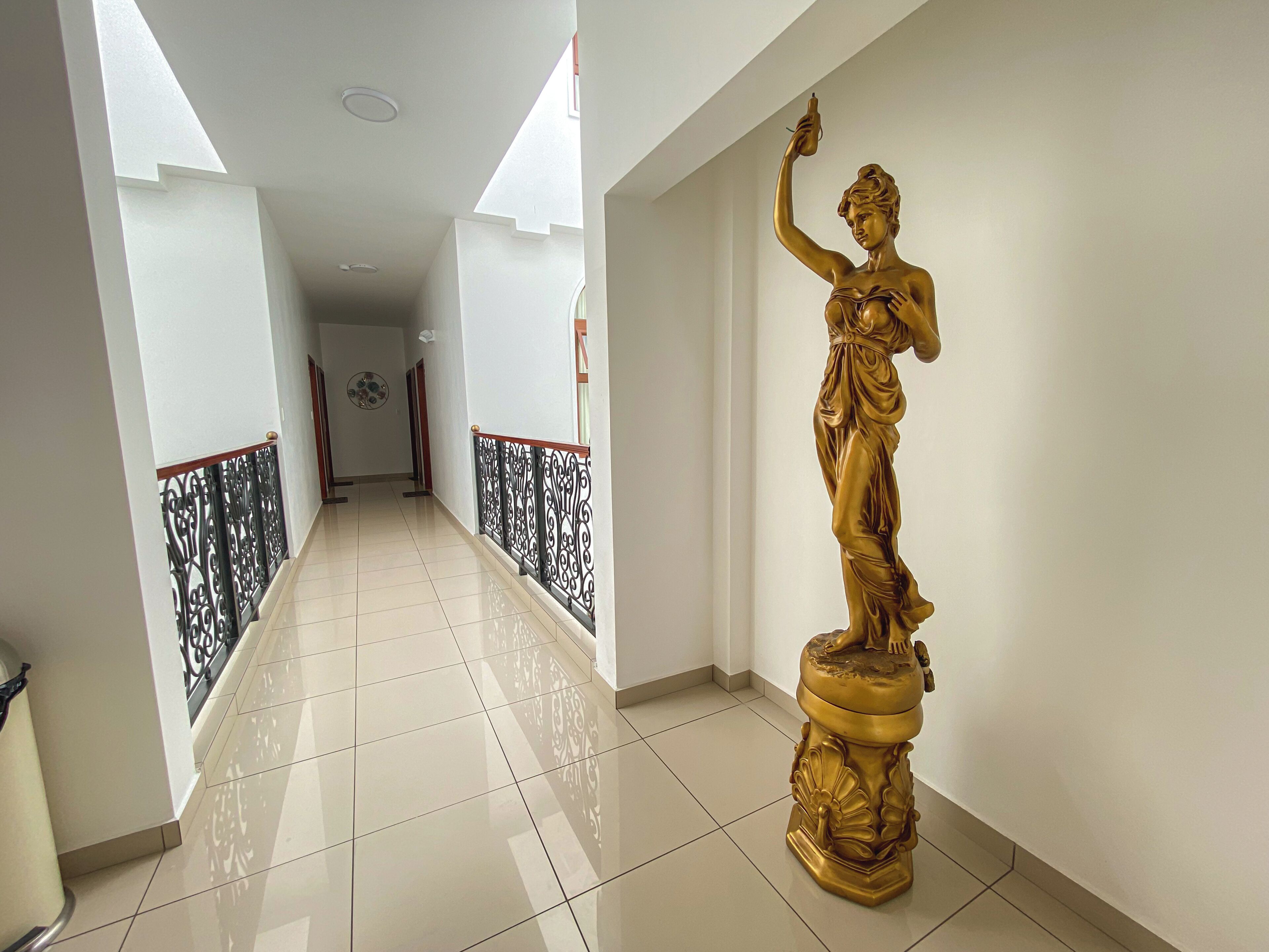 A hallway with a golden statue on a pedestal, white walls, and a tiled floor.