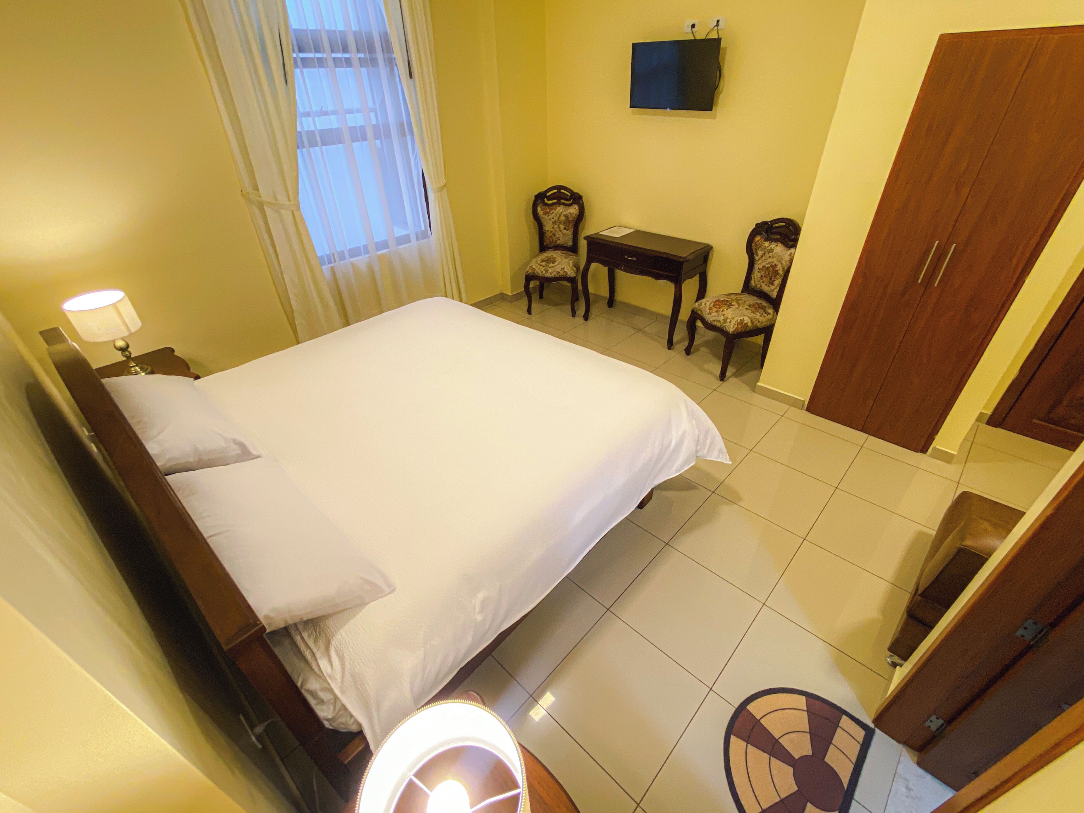 Una habitación de hotel con cama, escritorio, dos sillas, televisor y armario.