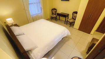 Una habitación de hotel con cama, escritorio, dos sillas, televisor y armario.