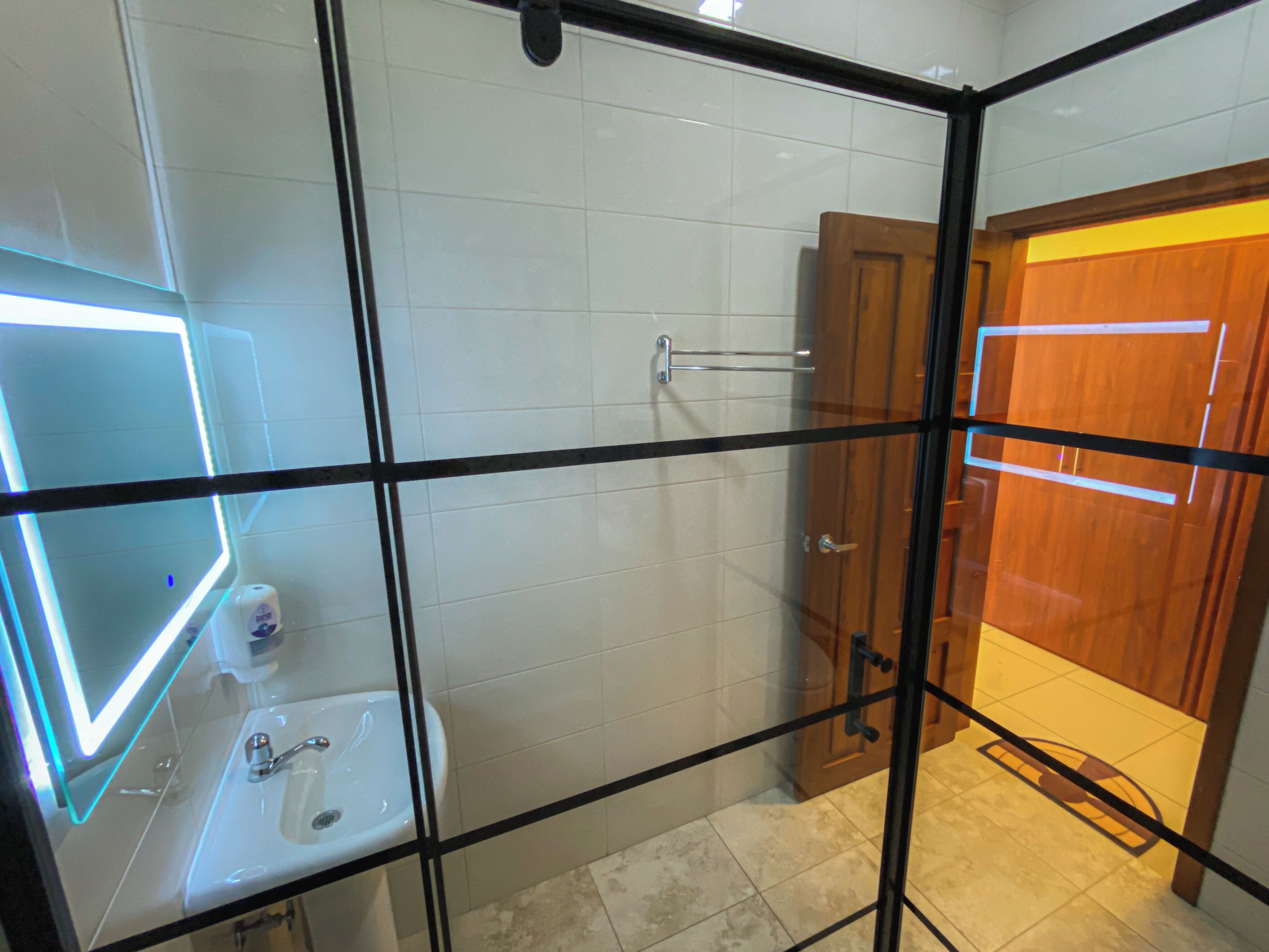 A bathroom with a glass partition, a sink, a mirror, and a shower area.