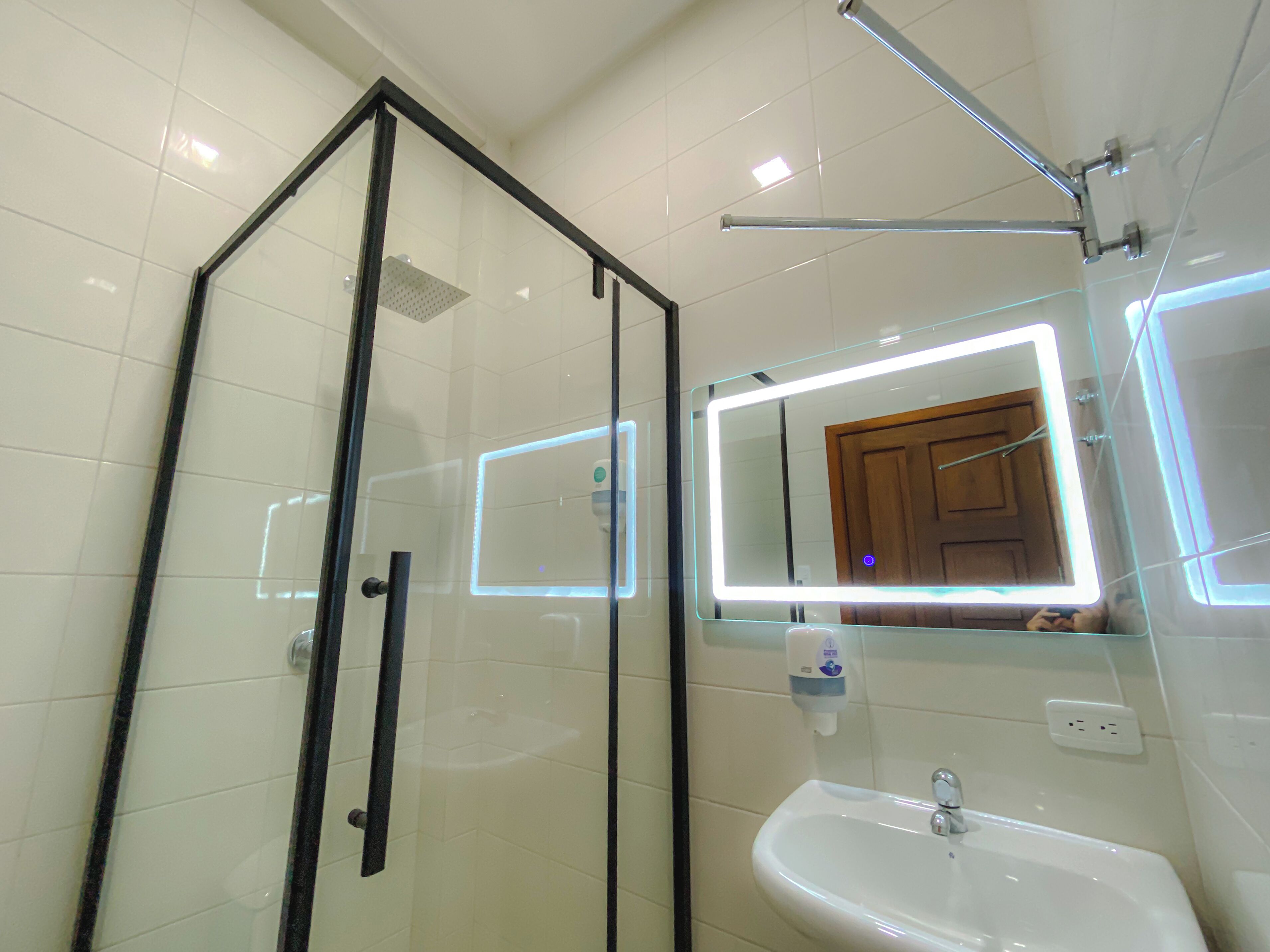 Un baño moderno con cabina de ducha de vidrio, un lavabo blanco e iluminación LED en el espejo.