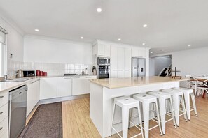 Eine moderne Küche mit weißen Schränken, einer zentralen Kochinsel mit Barhocker und einem Essbereich mit Tisch und Stühlen.