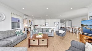 A modern living room with a grey sofa set, a wooden coffee table, and a dining area with white chairs. - Filoli - A breathtaking waterfront (Salamander Bay)