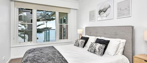 A bedroom with a large bed, a nightstand, a lamp, and a window with a view of trees and water.
