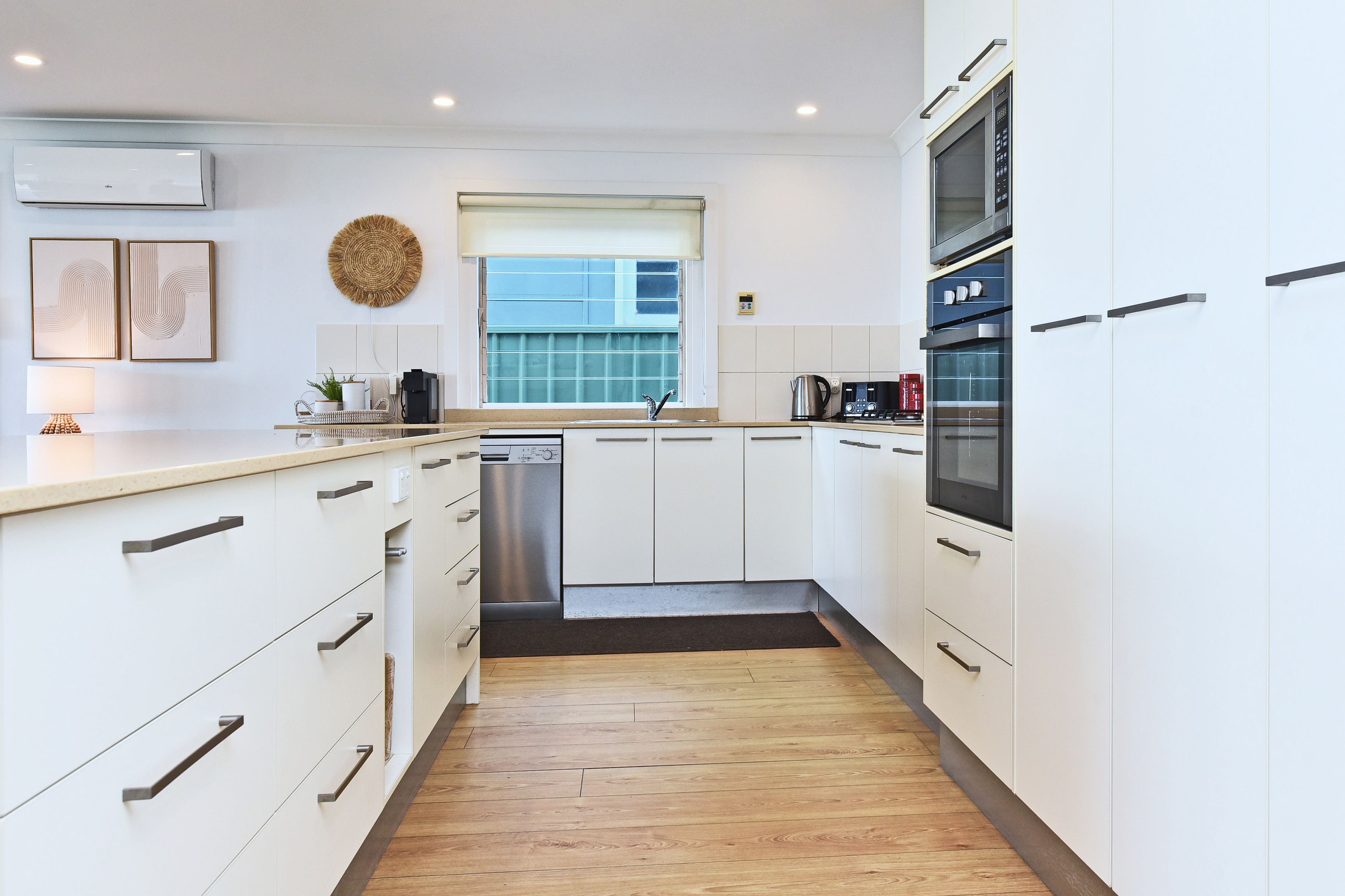 A modern kitchen with white cabinetry, stainless steel appliances, and a wooden floor.