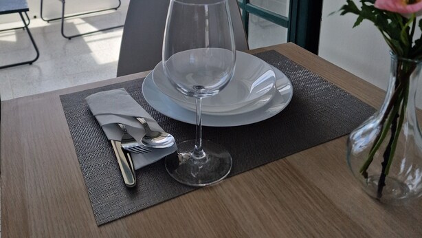Una mesa de comedor con una copa de vino, cubiertos y un florero con flores.