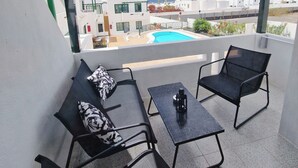 Un balcón con dos sillones, una mesita y una piscina al fondo.