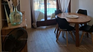 A dining area with a table and chairs, a vase with dried plants, and a view of a pool and greenery outside. - 4PA22 - Apartment in residence with pool and parking (COLLIOURE)