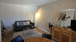 A modern living room with a round wooden dining table, a sofa, and a floor lamp. - 4PA22 - Apartment in residence with pool and parking (COLLIOURE)