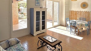A living room with a sofa, a cabinet, a table, and a dining area with chairs. - Pleasant village house close to the beach 4GSA12 (LE BARCARES)