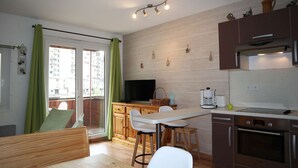 Una cocina moderna con armarios de madera, un comedor con mesa y sillas, horno empotrado y un amplio ventanal con cortinas.