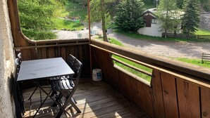Una terraza de madera con una mesa y sillas, con vistas a una zona boscosa y una carretera.