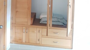 Un armario de madera con varios compartimentos, un espacio para colgar y una cama con edredón a cuadros.