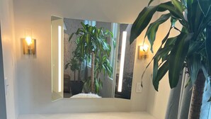 A modern bathroom with a large mirror, a white fluffy chair, and a potted plant. - The Hoosier House! An entire property experience! (Indianapolis)