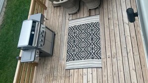 A wooden deck with a built-in grill, outdoor seating with wicker chairs, and a patterned rug. - The Hoosier House! An entire property experience! (Indianapolis)