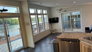Eine moderne Küche mit großem Fenster und Blick auf eine Terrasse, einem Geschirrspüler und einem an der Wand befestigten Flachbildfernseher.