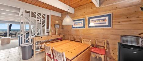 Un interior de madera con una mesa de comedor, sillas, una zona de cocina y vistas al exterior.