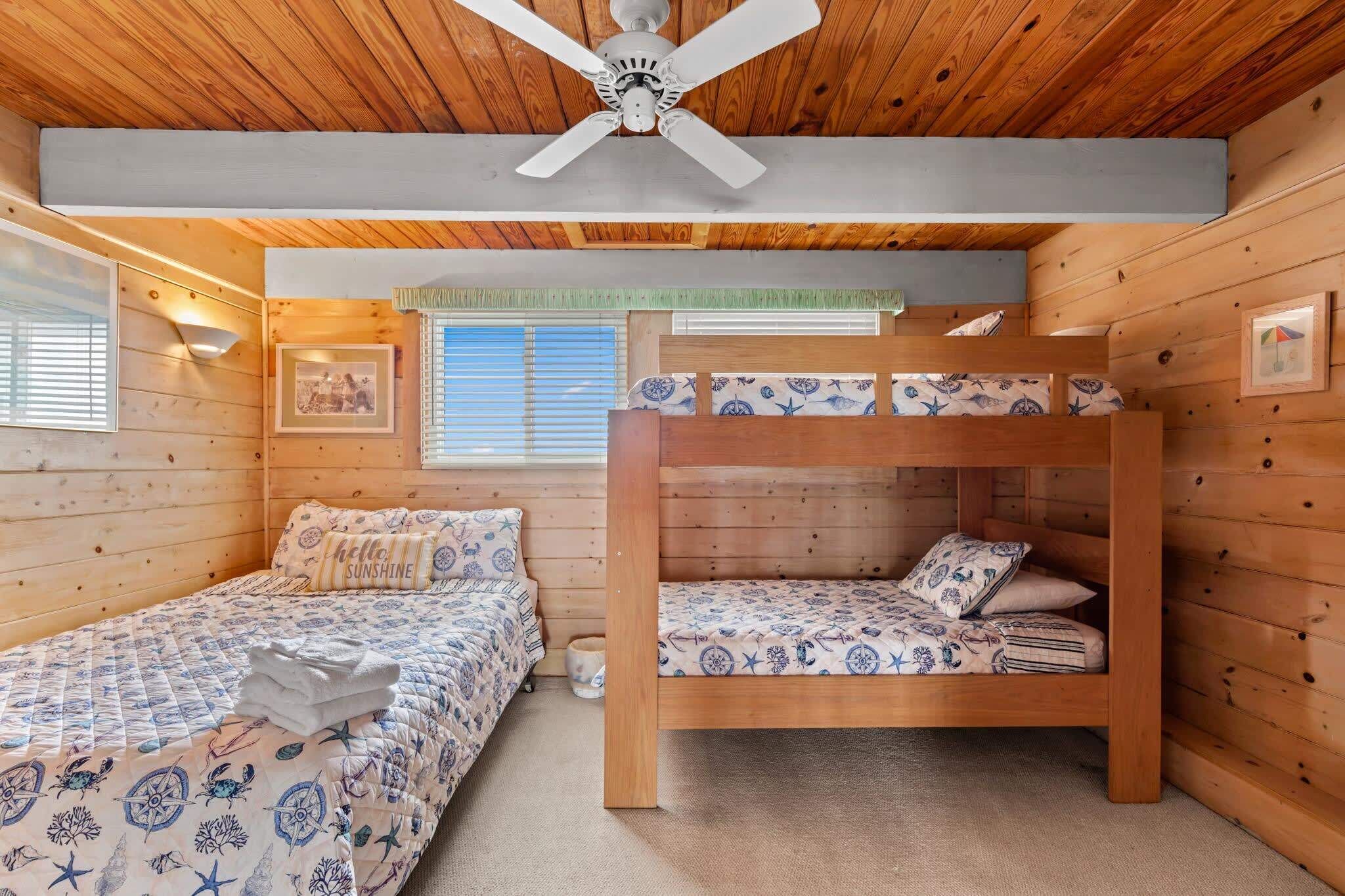 Une chambre de style cabane avec deux lits superposés, un ventilateur de plafond et des murs en bois.