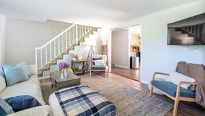 A spacious living room with a staircase, a sofa, a coffee table, and a TV mounted on the wall. - Perfect for Multiple Families- Close to Beach, Trails, Wineries, Breweries (South Haven)