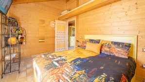 A wooden cabin room with a bed, a shelf with hats, and a door leading to another room. - Wooden house with porch and garden (Spoleto)