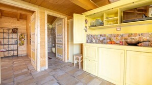 A kitchen with wooden cabinets, a tiled backsplash, and a small stool. - Wooden house with porch and garden (Spoleto)