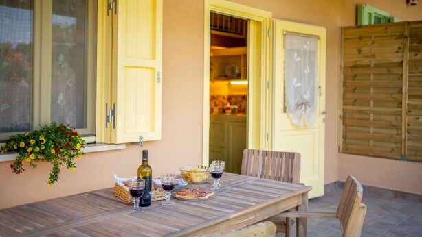 A wooden table with wine glasses and a bottle, set against a yellow wall with a window and a door. - Wooden house with porch and garden (Spoleto)