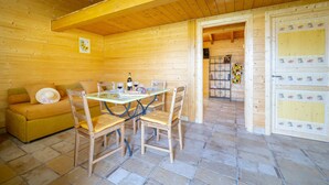 A wooden cabin interior with a dining table, chairs, a sofa, and a tiled floor. - Wooden house with porch and garden (Spoleto)