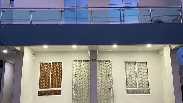 Ein modernes, zweistöckiges Gebäude mit Balkon, großen Fenstern und einem Beton-Erdgeschoss.