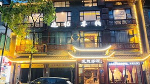 A multi-story building with traditional Chinese architectural elements, including a balcony with intricate lattice work and illuminated string lights. - zhuiyikezhan (Zhangjiajie)